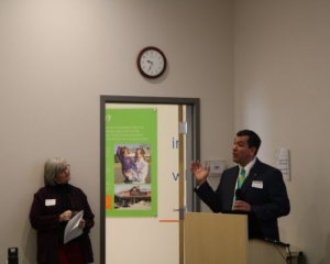 Photo of Green Bank President and CEO Bryan Garcia addressing the crowd while Inclusive Prosperity Capital's CEO Kerry O'Neill looks on.