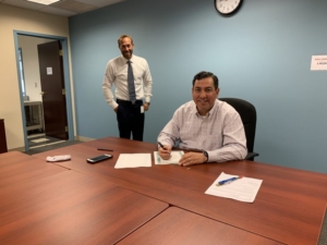 Photo of Green Bank President and CEO Bryan Garcia executes and signs the inaugural Green Liberty Bonds as Brian Farnen, Chief Legal Counsel, looks on.