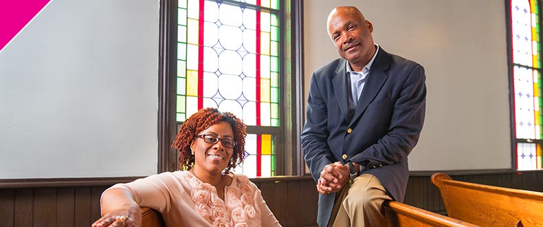 Man and woman sitting in church pew, smiling, looking at camera